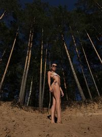 Portrait of young woman standing on sand in front of tall trees