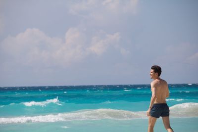 Shirtless man wading in sea against sky