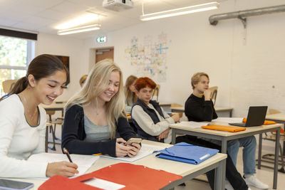 Teenage kids using phone and laptop in classroom