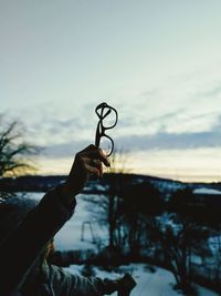 Person holding eyeglasses against sky during sunset