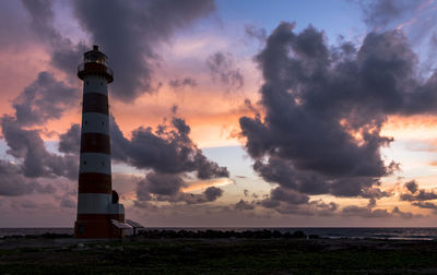 Lighthouse by sea against sky during sunset