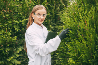 Young woman using phone while standing on plants