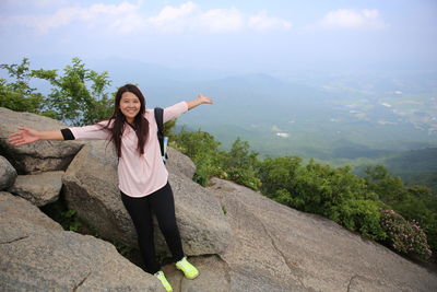 Woman with arms raised on mountain against sky