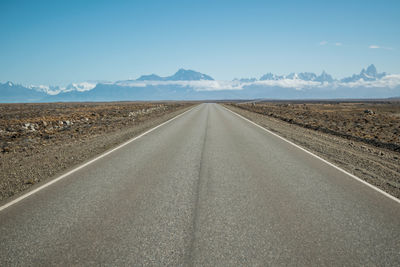Road leading towards desert and snowcapped mountains against sky