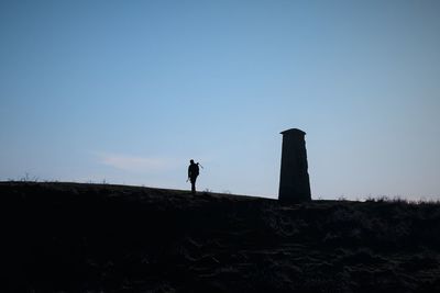 Silhouette photographer standing on a hill biside a tower against clear sky