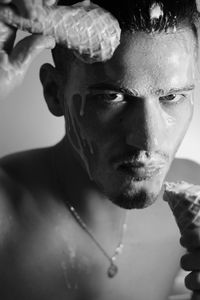 Close-up portrait of shirtless man face covering by ice cream indoors