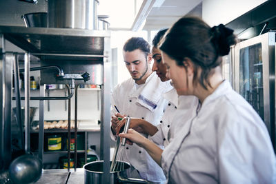 Female chefs cooking food while male colleague writing in notepad at commercial kitchen