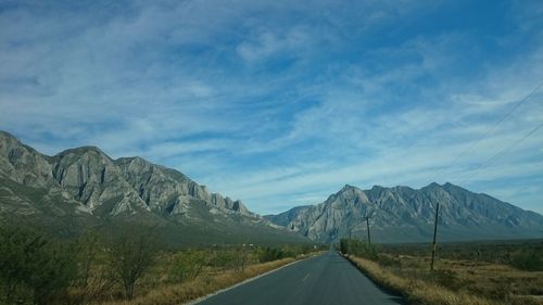 Road towards mountains against cloudy sky