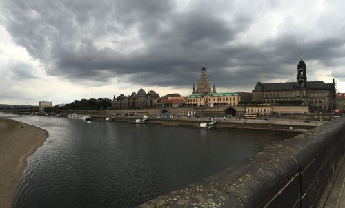 View of buildings by river against cloudy sky