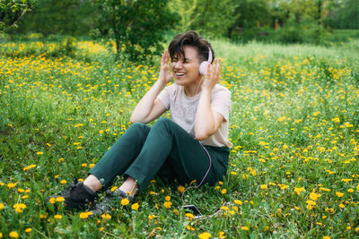 Young beautiful woman sitting on the lawn green grass with dandelions and listen to music 