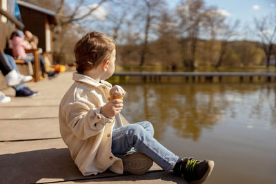 Little adorable boy sitting outdoors and eating ice cream. lake, water and sunny weather. 