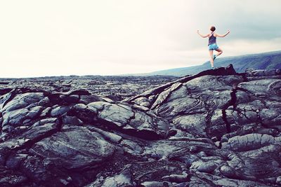 Rear view of woman exercising on rock against cloudy sky