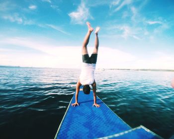 Man doing handstand on pier over sea against sky