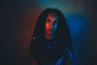 Portrait of young woman standing against black background