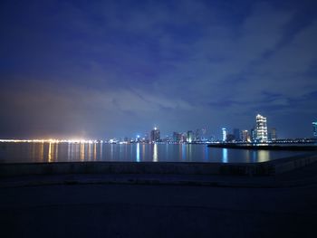 Illuminated cityscape by sea against sky at night