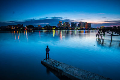 Silhouette man standing by sea against blue sky