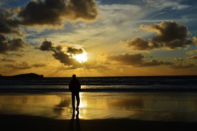Silhouette man walking on beach against sky during sunset