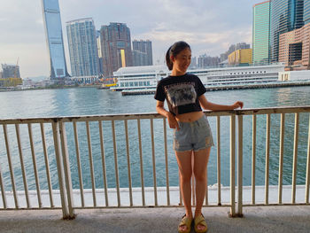 Side view of young woman standing against railing