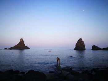 Couple standing at beach against blue sky during sunset