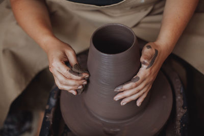 A middle-aged woman works on a potter's wheel, her face is not visible