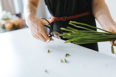 Midsection of florist cutting plant stems at table in shop