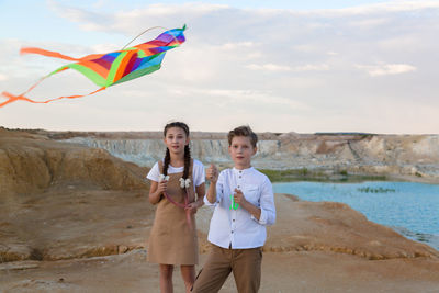 Brother and sister fly a kite standing near the river.