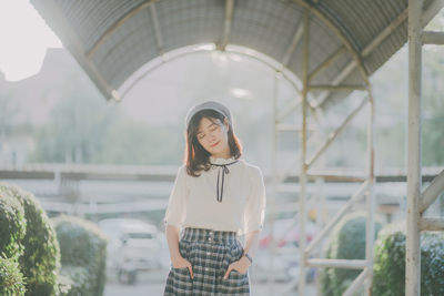Young woman standing on covered walkway against sky