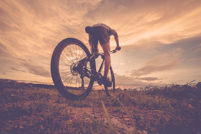 Low angle view of man riding bicycle against during sunset