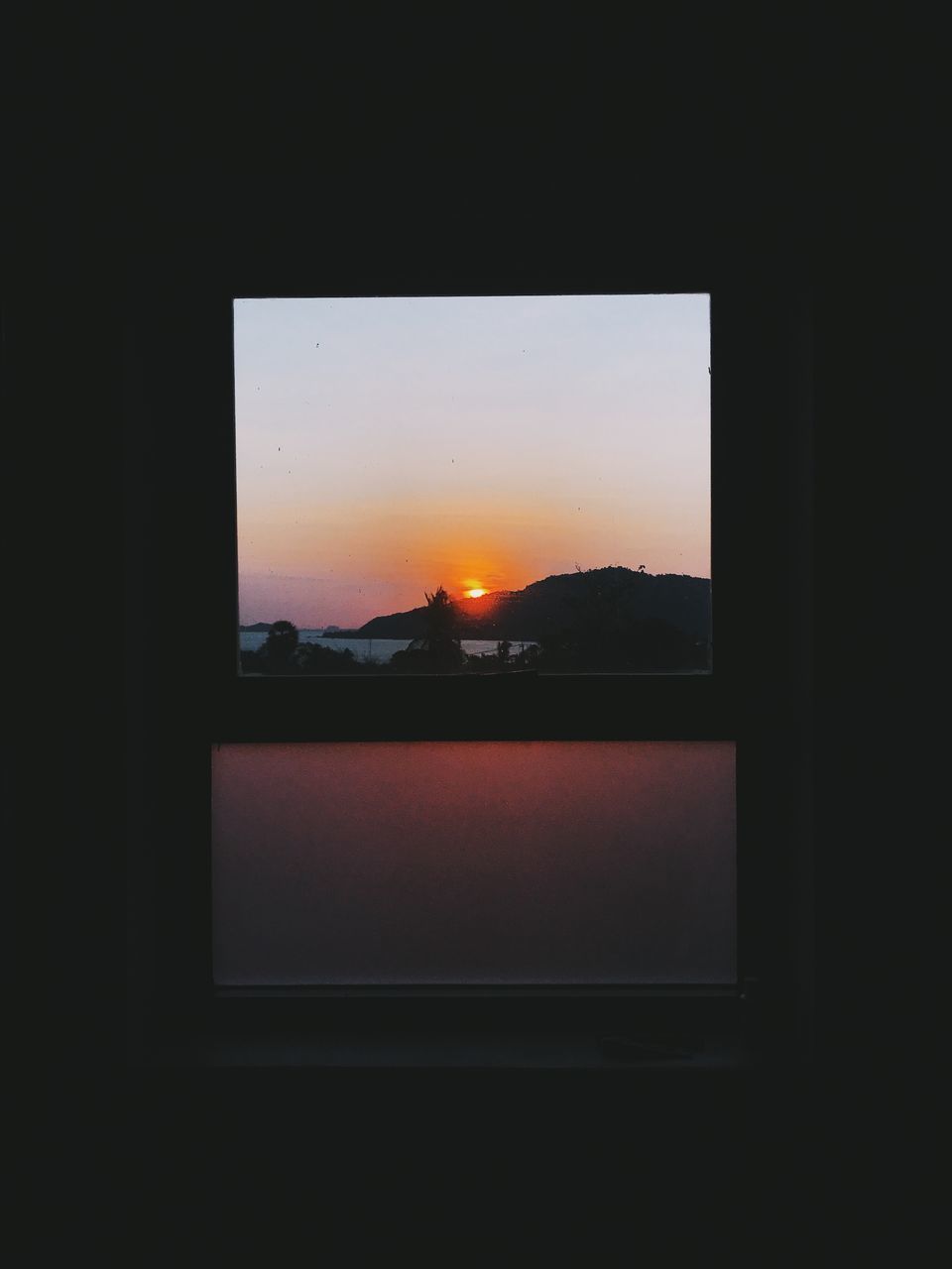 SILHOUETTE BUILDINGS AGAINST SKY DURING SUNSET SEEN THROUGH GLASS WINDOW