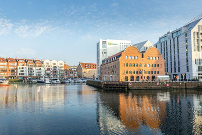 Buildings by river against sky in city