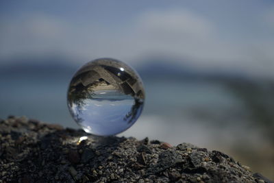 Close-up of crystal ball on rock against sea