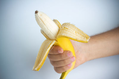 Cropped hand holding banana against white background