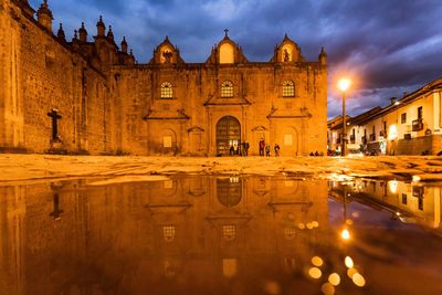 Reflection of illuminated church on puddle against cloudy sky at night