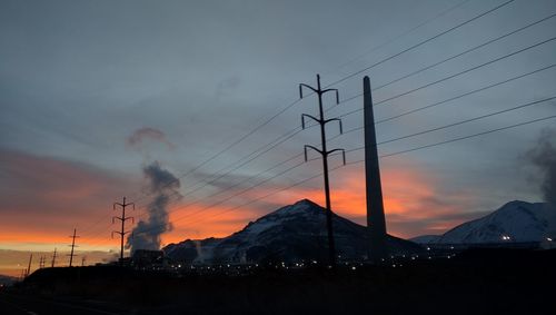 Low angle view of silhouette electricity pylons against sky