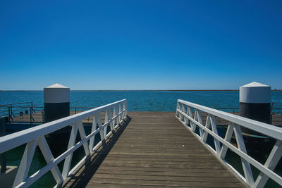 Pier on sea against clear blue sky