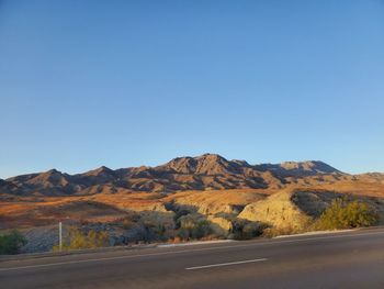 Scenic view of road and mountains against clear blue sky