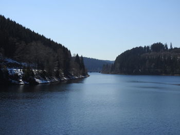 Scenic view of river by mountains against clear blue sky