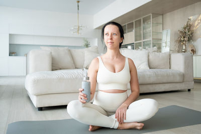 Pregnant woman holding bottle meditating at home