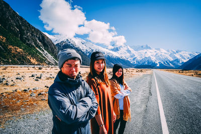 Portrait of smiling young woman standing on road against mountain