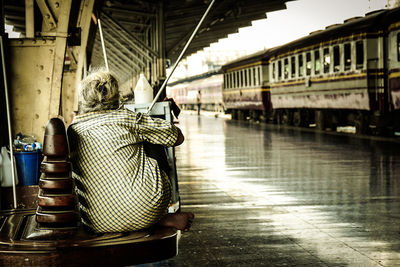 Rear view of woman sitting on seat at railroad station platform