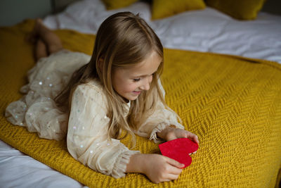 Cute smiling girl with heart shape lying on bed at home