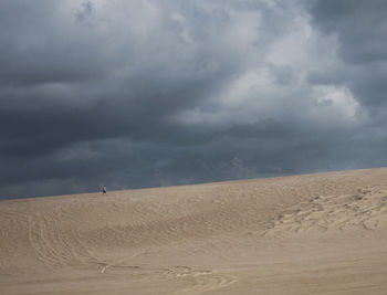 Sand dunes in desert against cloudy sky