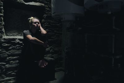 Sad woman sitting on seat by machinery at abandoned house