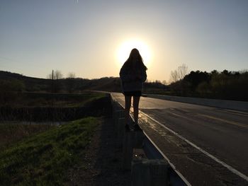 Rear view of woman standing on road against sky during sunset