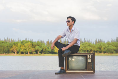 Side view of smiling teenage boy sitting on television set against sky