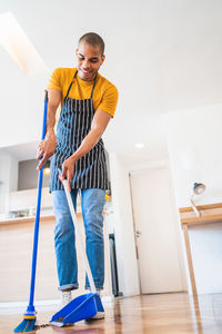 Mid adult man wearing apron while cleaning with equipment at home