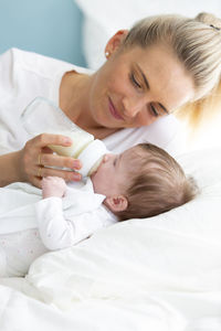 Mother feeding daughter on bed