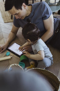 Father using digital tablet sitting with baby son at home