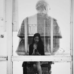 Reflection of young woman with mobile phone in front of man