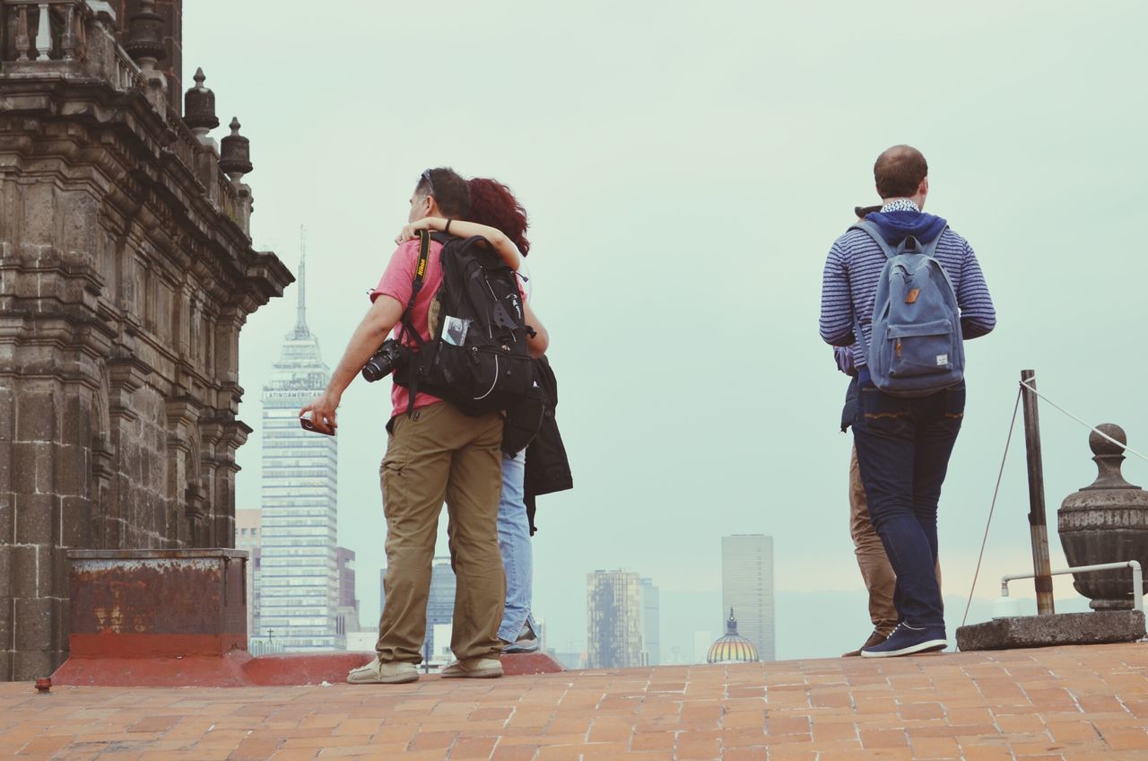 architecture, building exterior, built structure, casual clothing, clear sky, lifestyles, city, full length, leisure activity, standing, day, young adult, outdoors, men, low angle view, copy space, tourism, rear view